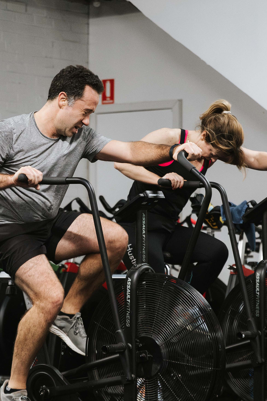Two members working through an air bike effort side by side