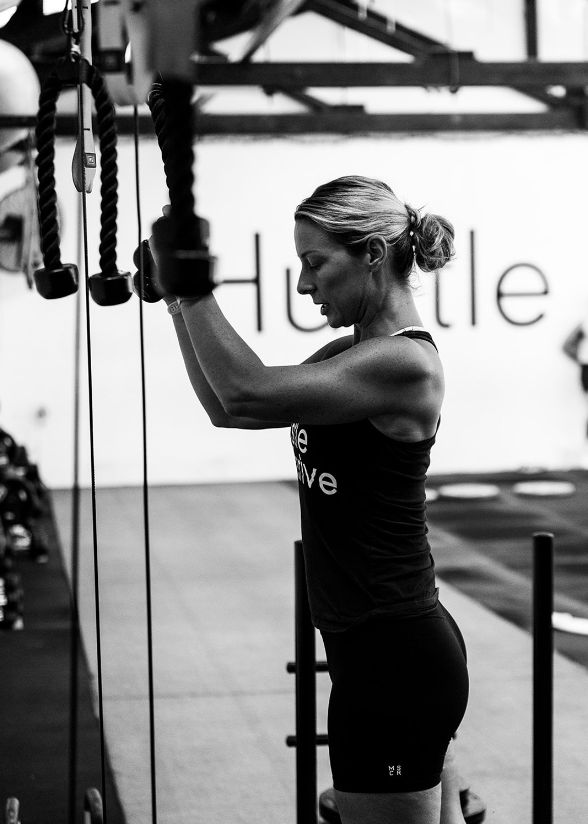 Member training on a cable machine beneath the Hustle & Thrive wall branding
