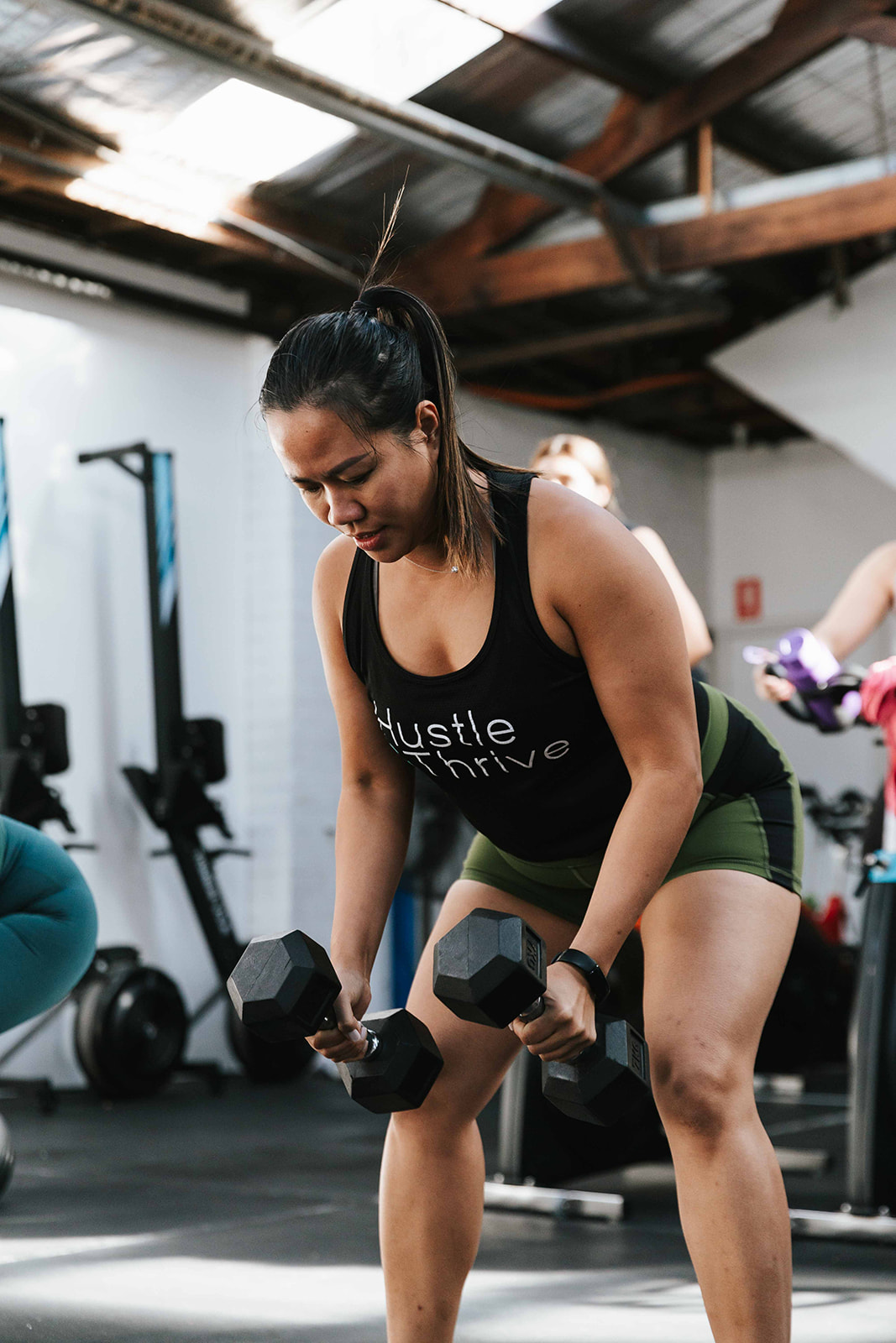 Member rowing dumbbells in a Hustle and Thrive singlet