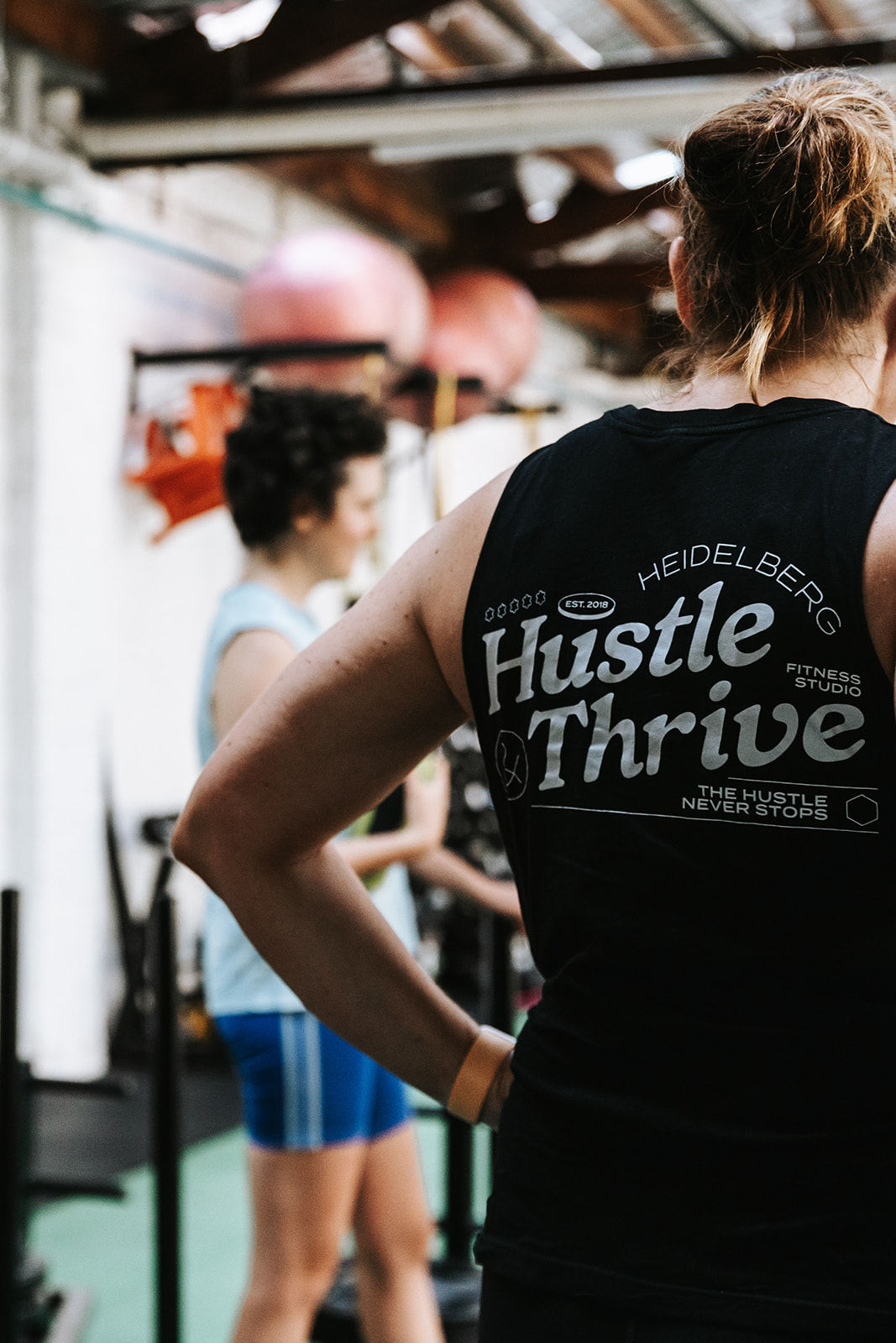 Member in a Hustle & Thrive Heidelberg singlet watching a class from the gym floor