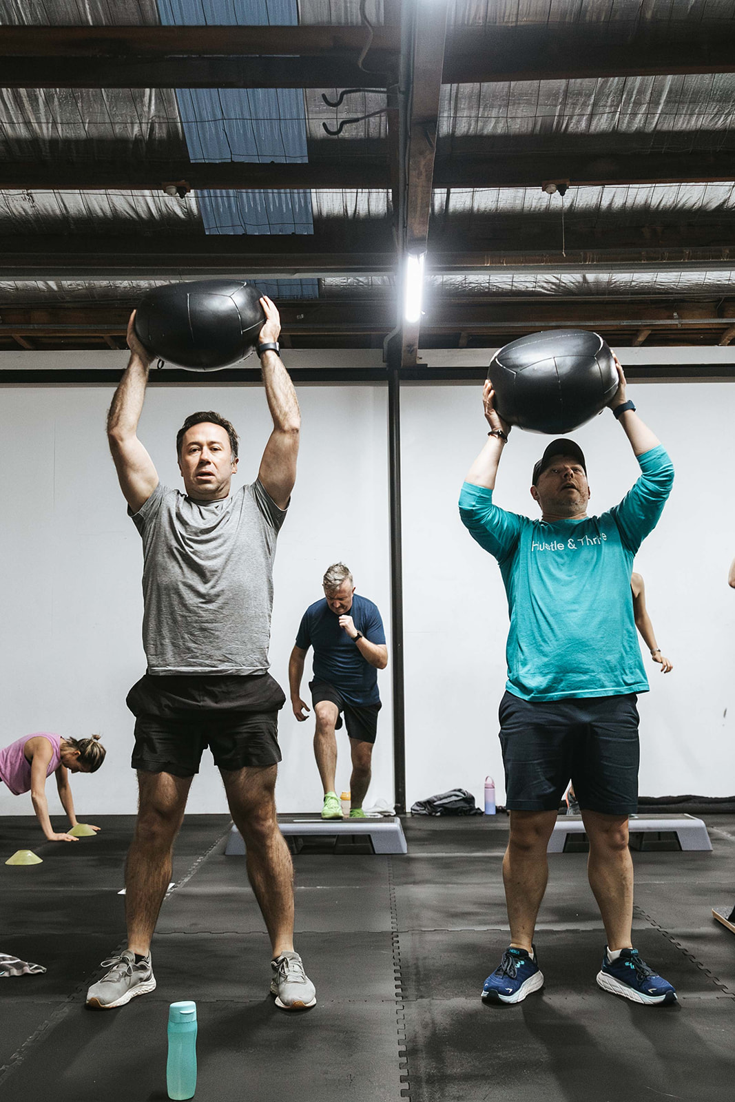 Two members pressing slam balls overhead in a group session
